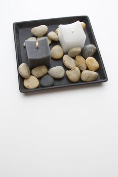 Dark grey and white candle in a plate with rounded rocks