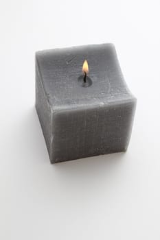 lit square gray candle against white background