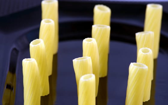 Three rows of maccheroni standing on a black plate