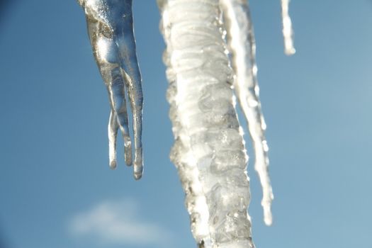 Icicle hanging against a blue sky with sunlight shinning through them.