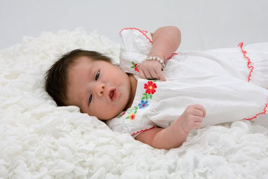 Baby with brown hair laying on white blanket