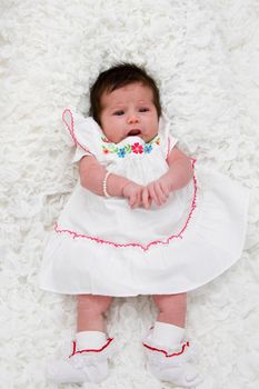 Baby with brown hair laying on white blanket