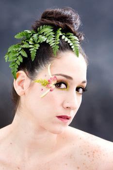 Beautiful brunette face with pink green yellow eye flower petal makeup, isolated on gray