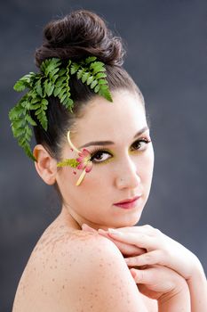 Beautiful brunette face with pink green yellow eye flower petal makeup, isolated on gray