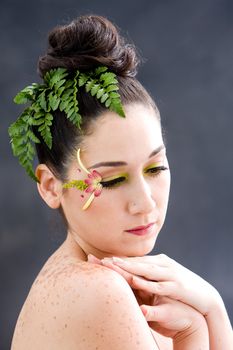 Beautiful brunette face with pink green yellow eye flower petal makeup, isolated on gray