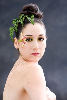 Beautiful brunette face with pink green yellow eye flower petal makeup, isolated on gray
