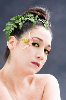 Beautiful brunette face with pink green yellow eye flower petal makeup, isolated on gray