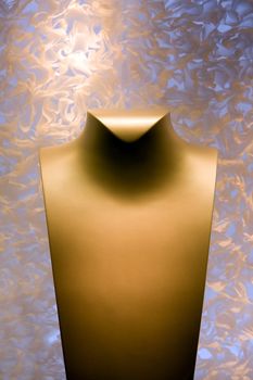 A golden yellow color neck form for display of necklace jewelry on a fluffy background