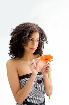 Beautiful young woman with brown curly wild hair and orange flower in hand pulling petals, isolated