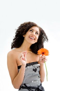 Smiling happy beautiful young woman with brown curly wild hair and orange flower in hand and pulling petals, isolated