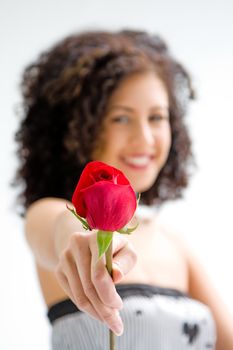 Sincere beautiful young woman with brown curly wild hair and bare shoulders presenting red rose, isolated