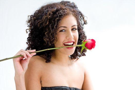 Sincere beautiful young woman with brown curly wild hair and bare shoulders biting rose, isolated