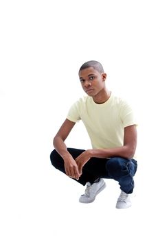 Casual young African man in yellow shirt and jeans squatting, isolated