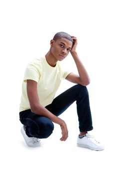 Casual young African man in yellow shirt and jeans squatting and worried, isolated