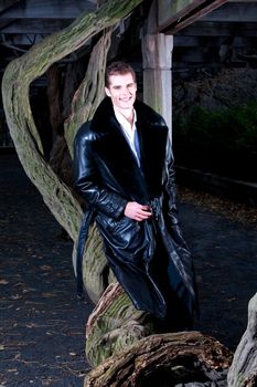 Handsome Caucasian guy leaning against a vine tree under a pergola at night