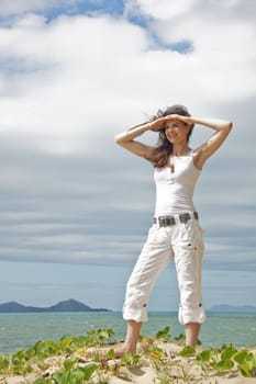 A fit and attractive woman standing on a sand dune looking out over a tropical beach