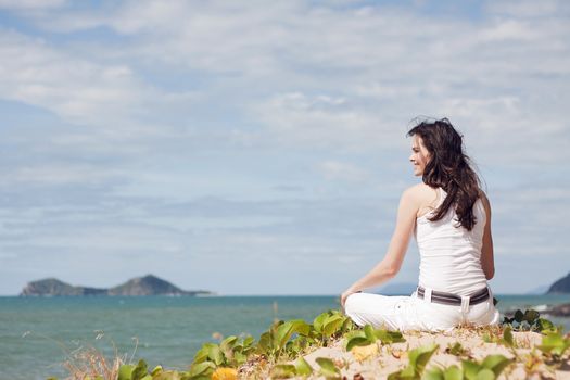 An attractive woman sitting down relaxing on top of a sandune on a tropical beach 