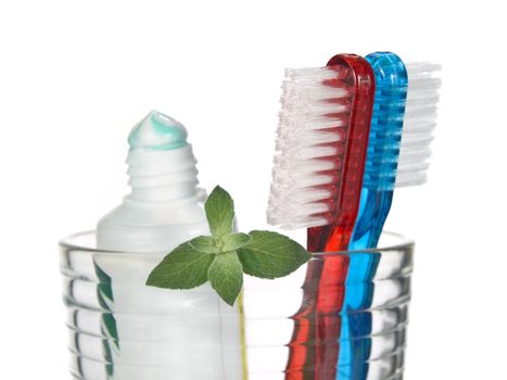 Toothbrushes, toothpaste and mint leaves in a glass over white background.