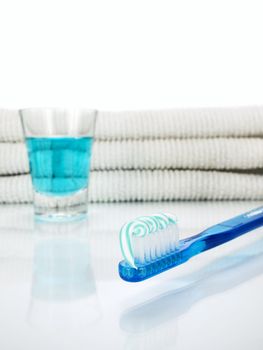 A blue toothbrush with toothpaste, a glass full of mouthwash and towels on the background.