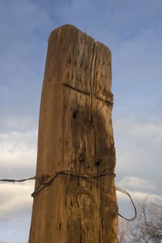 solid wooden fence post (railroad tie)  with a barbed wire attached against blue sky and clouds