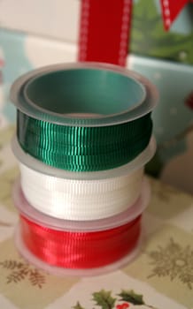 Three spools of Christmas gift wrapping ribbon sitting on already wrapped gifts.
