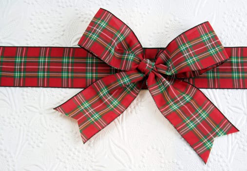 A plaid christmas bow on decorative white paper.
