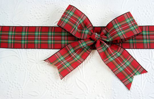 A plaid christmas bow on decorative white paper.