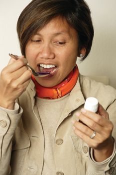 An Asian female in her early 40's taking a spoonful of cough medicine.
