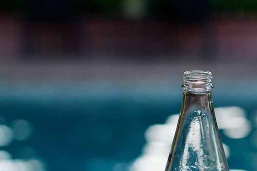 Top of empty glass bottle against a soft background of a pool