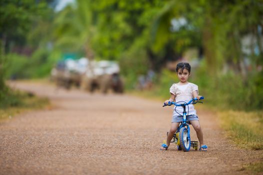 cute thai-indian girl riding her bike on a dirt road. focus on the girl with a shallow depth of field and lot of free space.