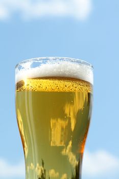 Closeup of beer glass with foam on blue sky background