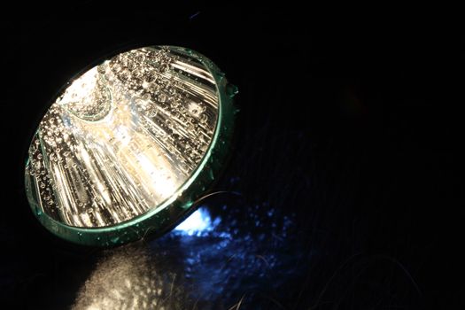 Closeup of luminous flashlight and water drops on dark background