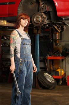 Photo of a young beautiful redhead mechanic wearing overalls and holding a huge wrench.  Attached property release is for arm tattoos.

