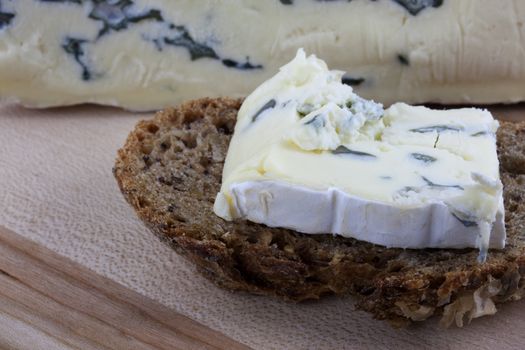 slice of whole grain wheat bread with soft blue, Gorgonzola cheese on wooden cutting board with cheese wedge in background