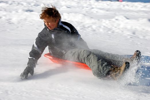 Boy braking while sledding down the hill with snow background