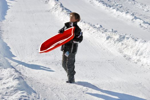 boy carrying his sled down the hill with snow background