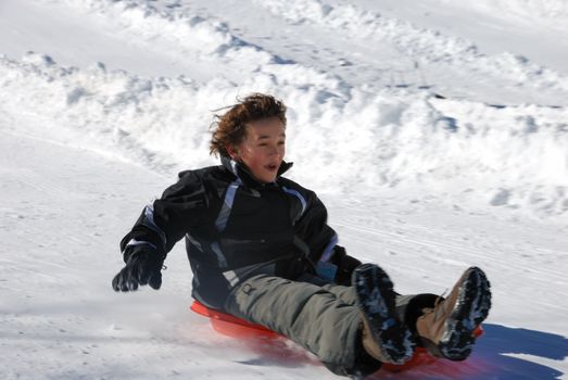 boy sledding fast down the hill on a red sled with snow background