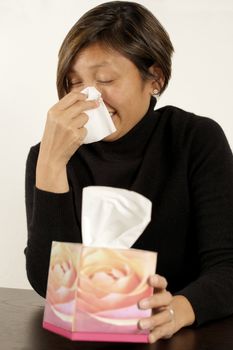 Asian woman sneezing or blowing her nose.  Design on tissue box is one of my flower images in my portfolio.
