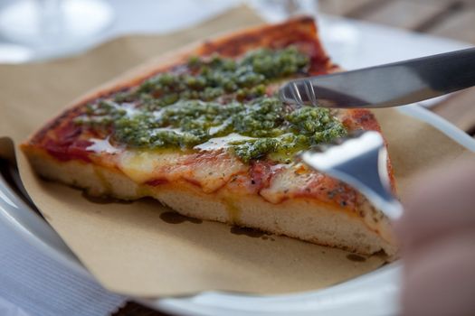 Delicious slice of pizza with pesto and mozarella on top with knife and fork
