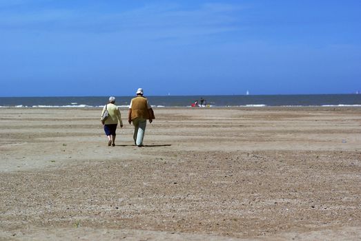 Elderly couple walking on the beach on a sunny day.