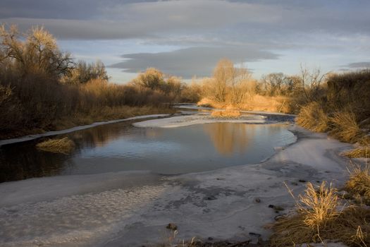small river, Cache la Poudre below Fort Collins, Colorado, paritally frozen with low flow on winter sunset