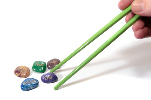 five stones inscribed hope joy peace faith and believe being picked up by chopsticks showing have belief with shadows