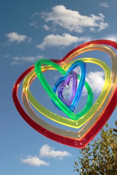 six heart shaped plastic pieces one inside the other on a cloudy sunny background hanging by a thread