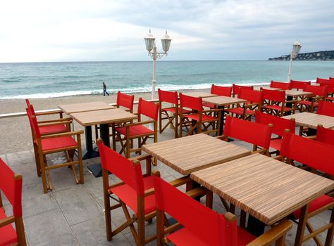 Terrace made of red chairs, black tables and old looking lamps near the beach and the mediterranean sea at Menton, south of France