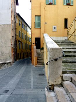 Stairs, street and orange buildings with green shutters in old city of Menton, south of France