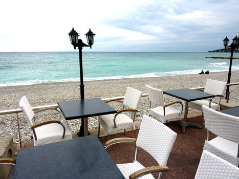 Terrace made of white chairs, black tables and old looking lamps near the beach and the mediterranean sea at Menton, south of France