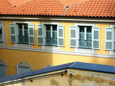 Red roof of an orange building with green shutters in front of a banister in old city of Menton, south of France, by sunny day
