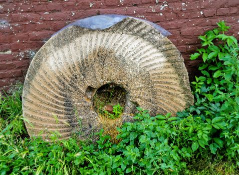 Old broken mill stone at the foot of a closed windmill