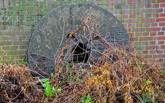 Old broken mill stone at the foot of a closed windmill