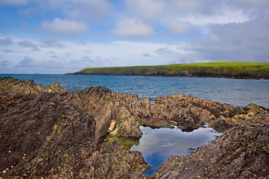 A rock pool with the sea and cliffs behind